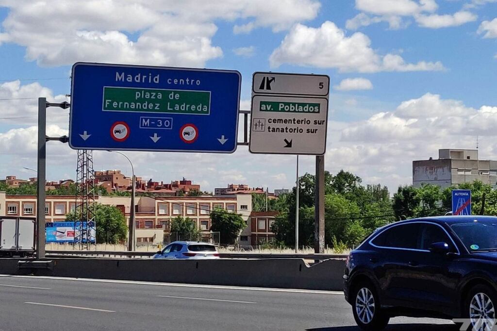 imagen de una calle con trafico y un letrero que dice zona de bajas emisiones madrid con un automovil electrico pasando