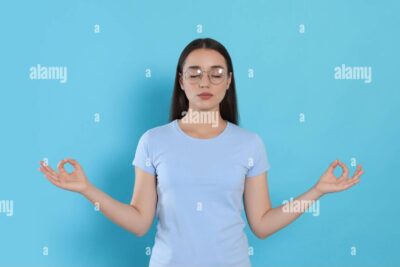 una mujer con expresion de paz mental meditando en un jardin rodeado de naturaleza